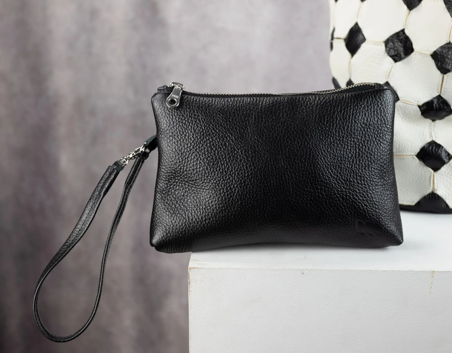 Black leather clutch bag on a white surface with a patterned wall in the background
