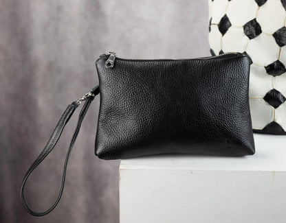 Black leather clutch bag on a white surface with a patterned wall in the background