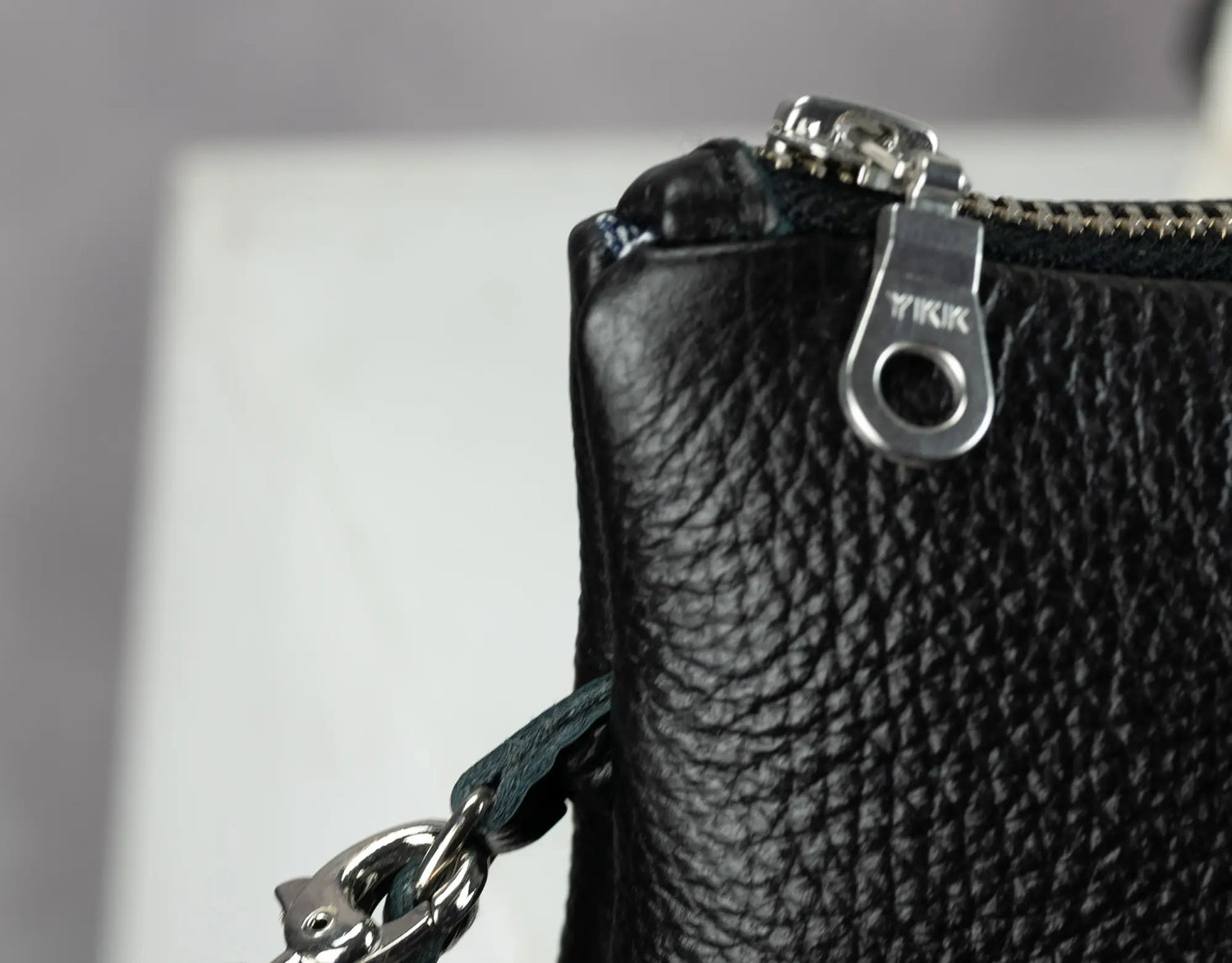 Close-up of a black leather wallet with a silver zipper on a light gray background