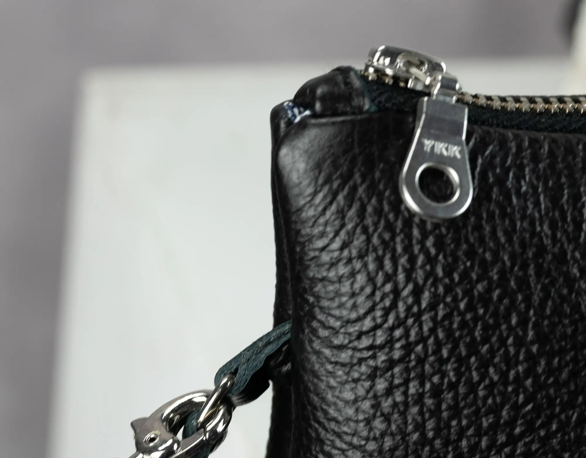 Close-up of a black leather wallet with a silver zipper on a light gray background