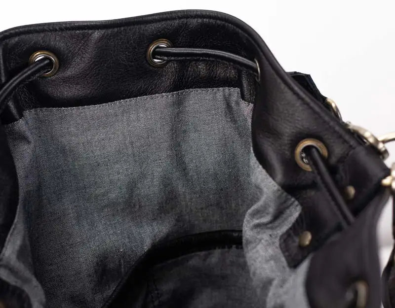 Close-up of a black leather bag with drawstring and metal eyelets on a white background