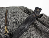 Close-up of a textured fabric bag with a black strap and gold zippers on a white background
