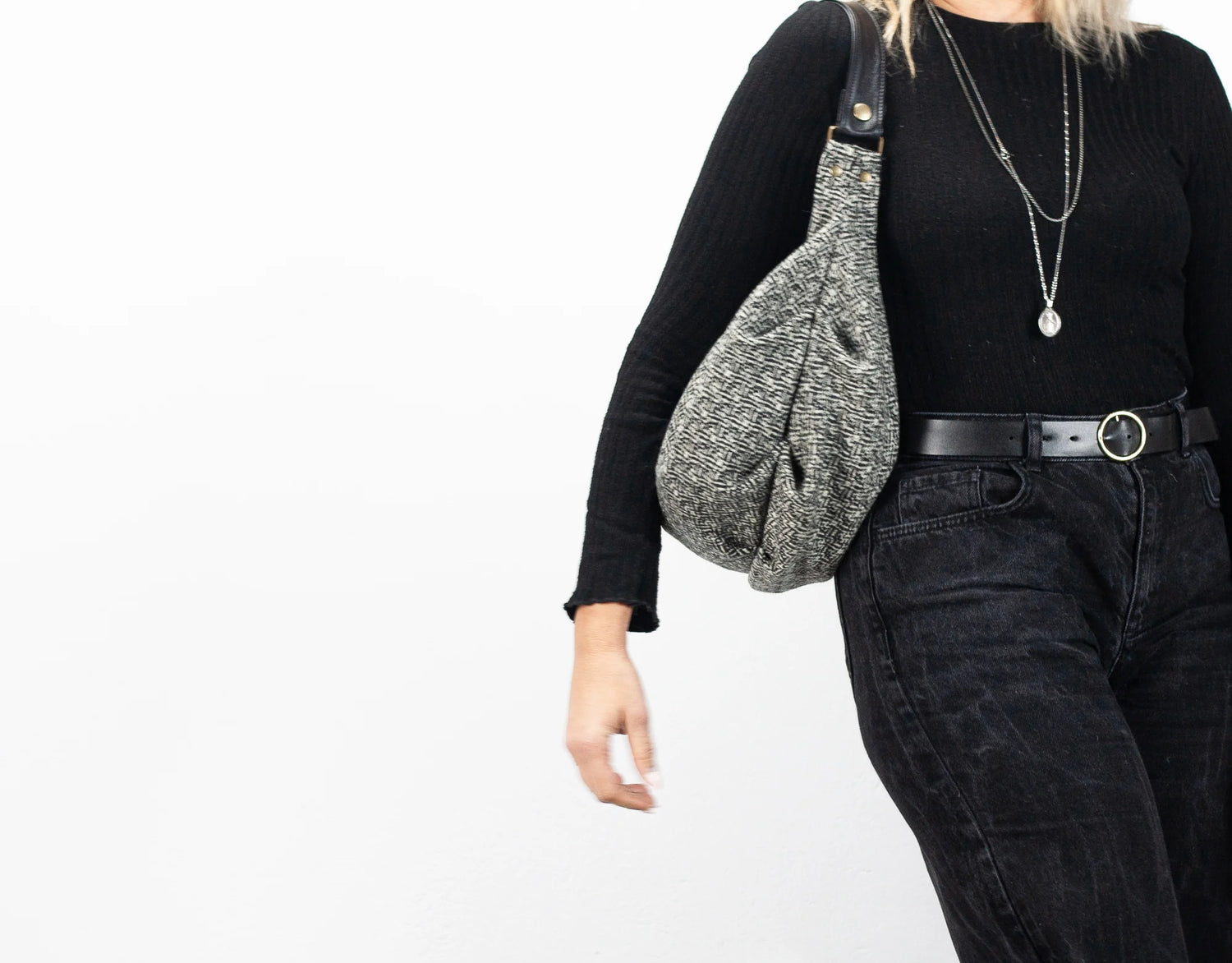 Person wearing a black long-sleeve top and dark jeans, holding a gray textured bag on a white background