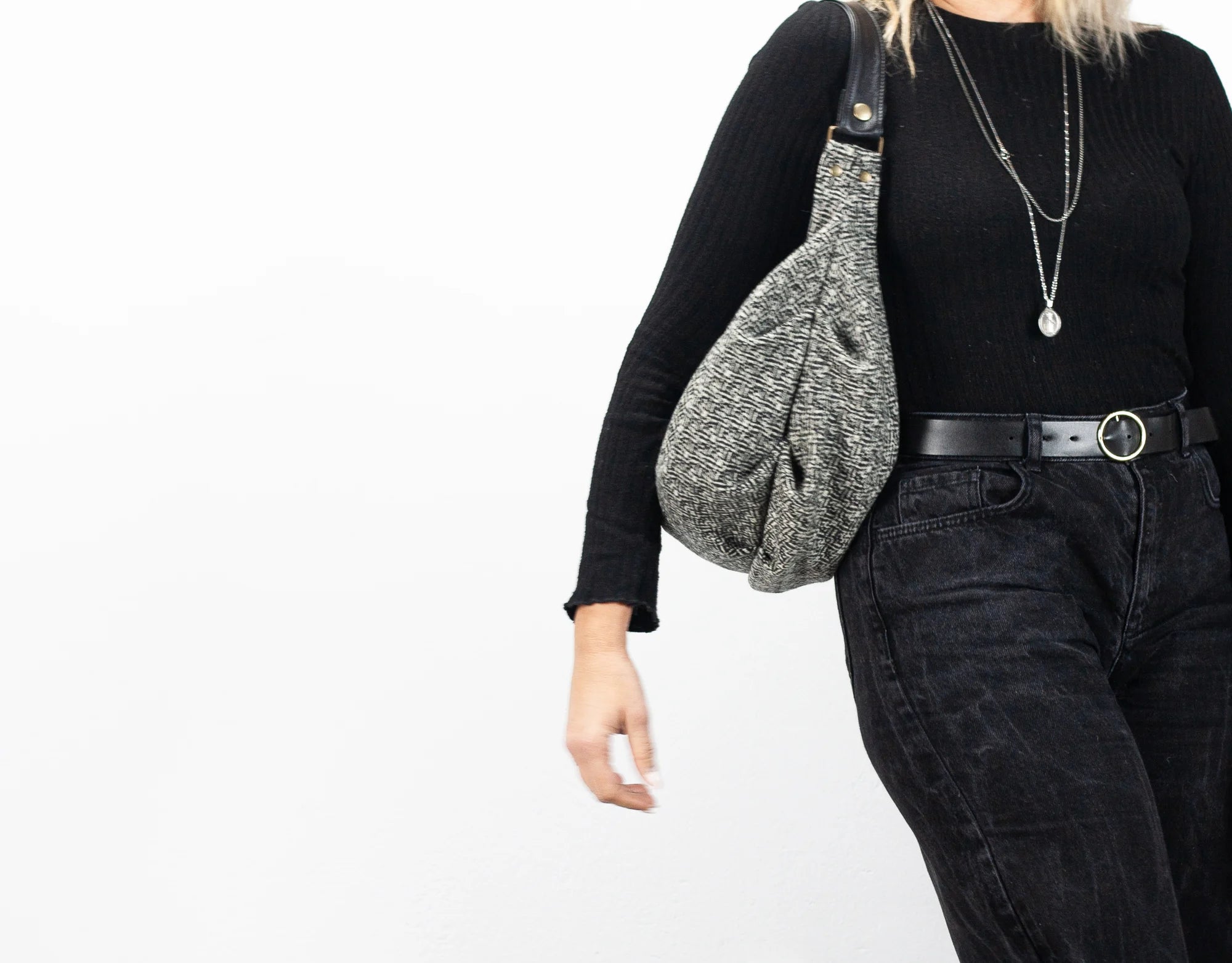 Person wearing a black long-sleeve top and dark jeans, holding a gray textured bag on a white background