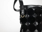 Close-up of a black woven leather handbag with a hexagonal pattern, a black leather strap, and a small gold-tone metal ring on a white background.