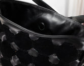 Close-up of a black leather handbag with a textured woven or embossed pattern on the front, showing the interior lining and a metal grommet.