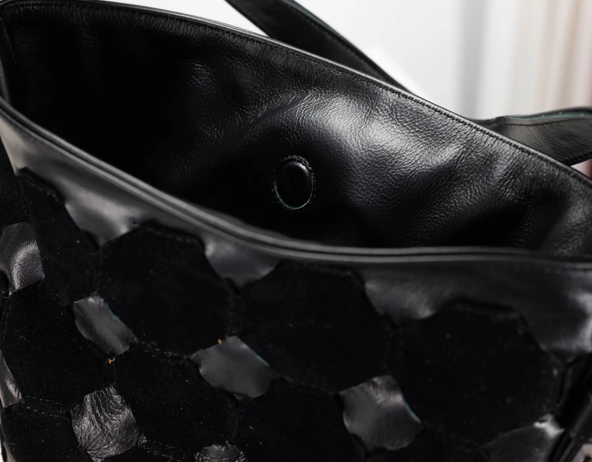 Close-up of a black leather handbag with a textured woven or embossed pattern on the front, showing the interior lining and a metal grommet.