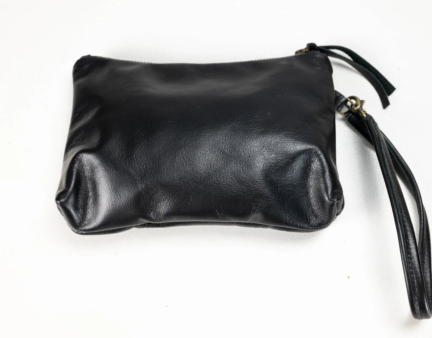 Black leather wristlet clutch with a zipper closure and wrist strap, photographed on a plain white background.