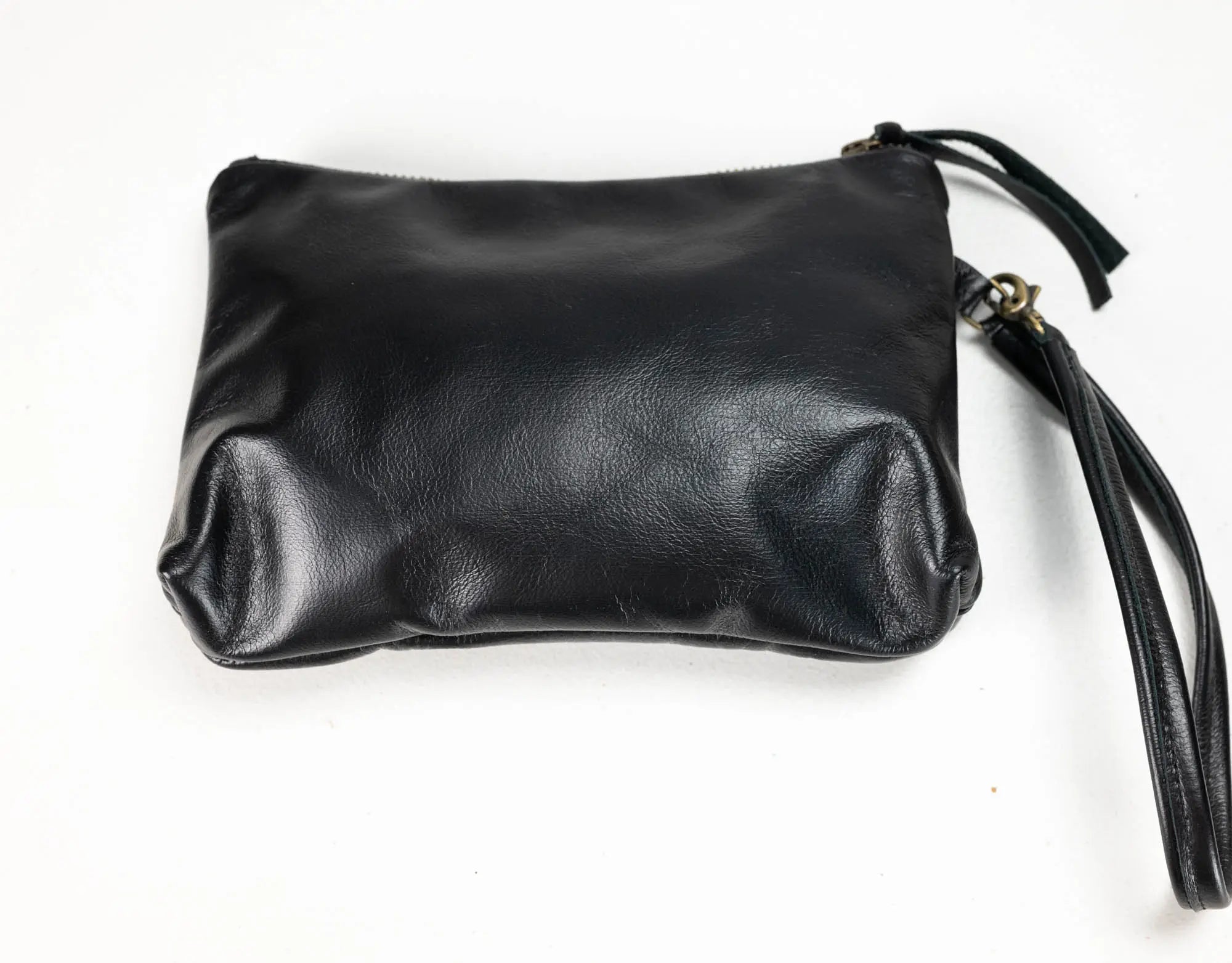 Black leather wristlet clutch with a zipper closure and wrist strap, photographed on a plain white background.
