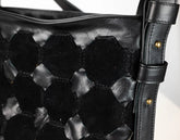 Close-up of a black woven leather shoulder bag with a hexagonal pattern and a matching strap featuring brass-tone rivets.