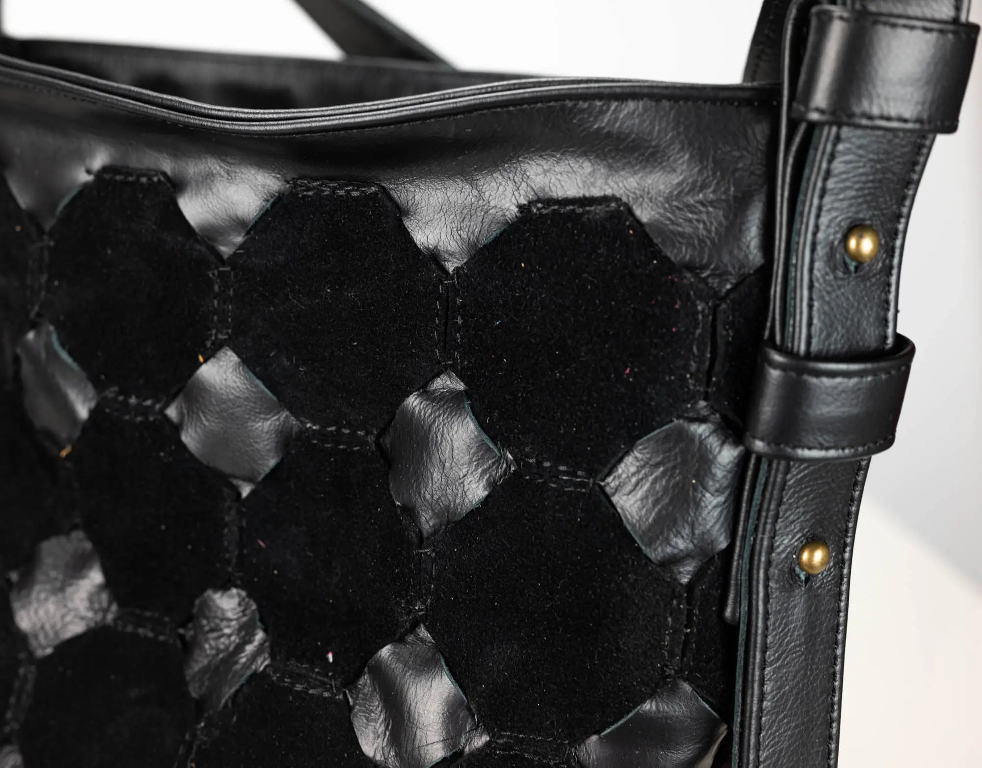 Close-up of a black woven leather shoulder bag with a hexagonal pattern and a matching strap featuring brass-tone rivets.