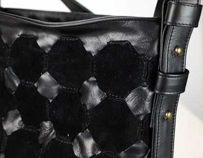 Close-up of a black woven leather shoulder bag with a hexagonal pattern and a matching strap featuring brass-tone rivets.