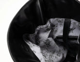 Close-up of the interior of a black leather bag, showing a white lining with a black floral and bird pattern and a black strap.
