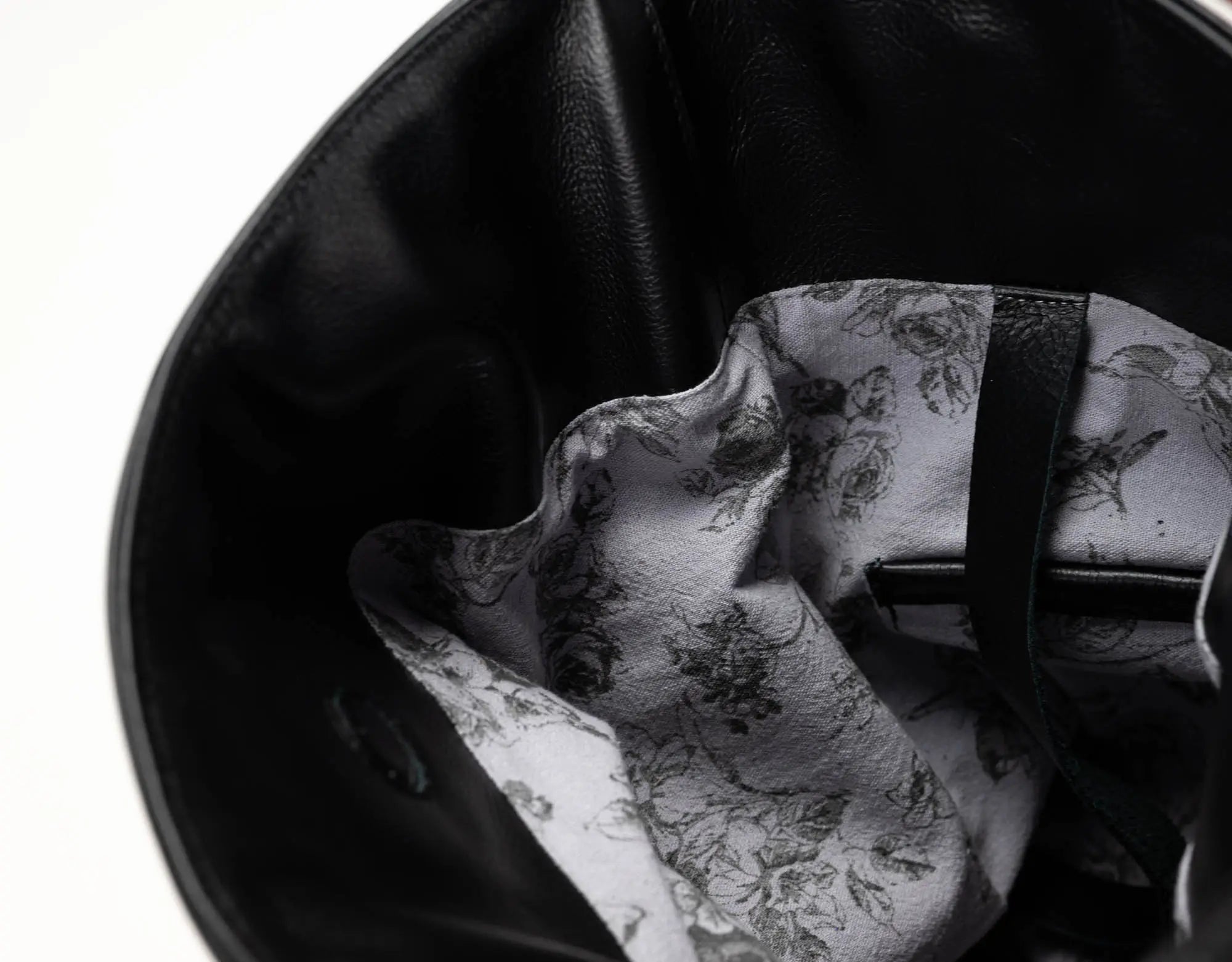 Close-up of the interior of a black leather bag, showing a white lining with a black floral and bird pattern and a black strap.