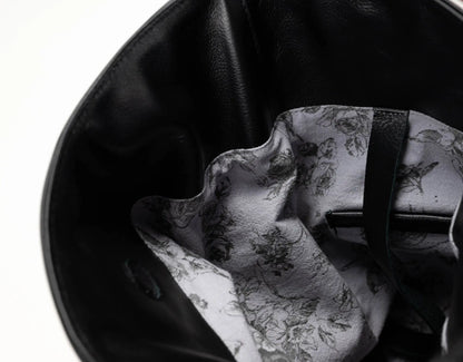 Close-up of the interior of a black leather bag, showing a white lining with a black floral and bird pattern and a black strap.