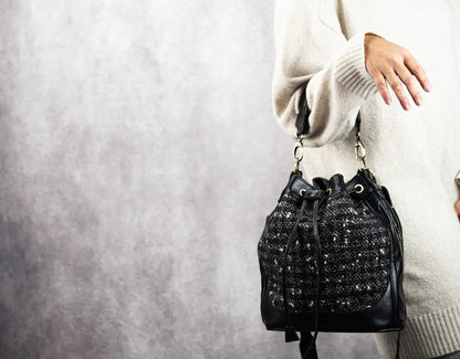 Black textured handbag held by a person wearing a light-colored sweater against a neutral background