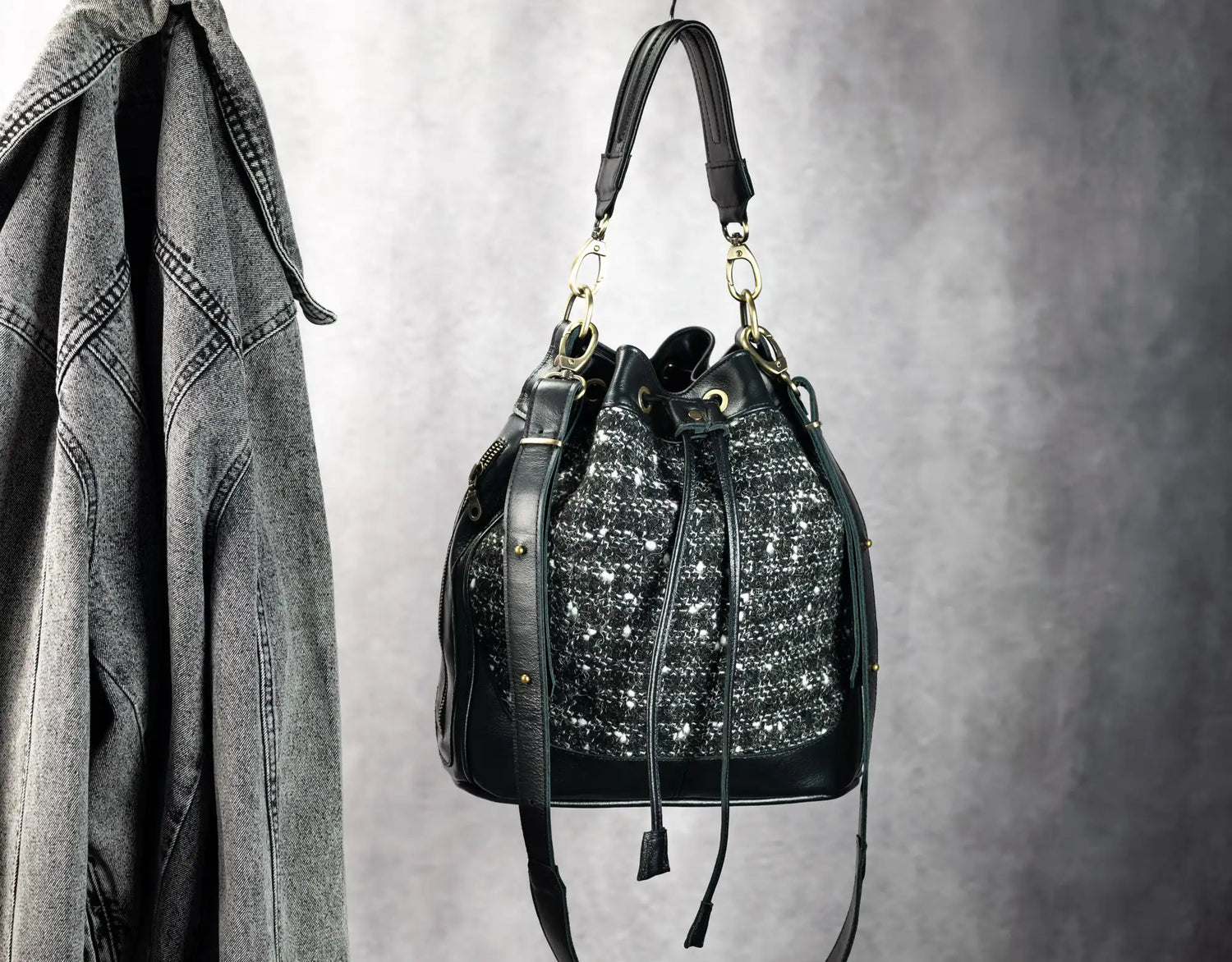Black handbag with decorative elements hanging on a hook against a gray background