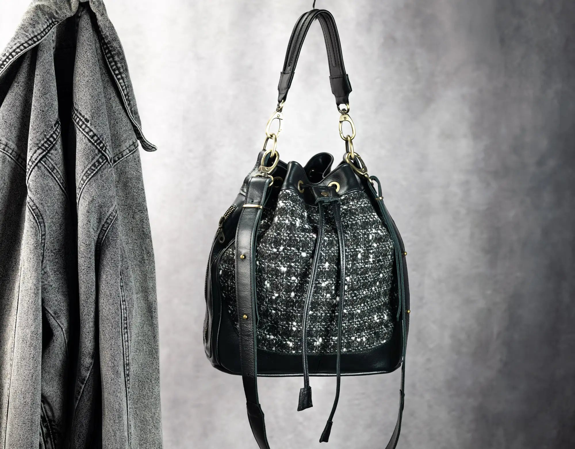 Black handbag with decorative elements hanging on a hook against a gray background