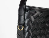 Close-up of a black woven handbag with a gold clasp on a white background
