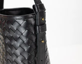 Black woven leather handbag with a strap on a white background