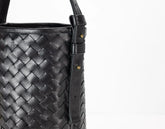 Black woven leather handbag with a strap on a white background
