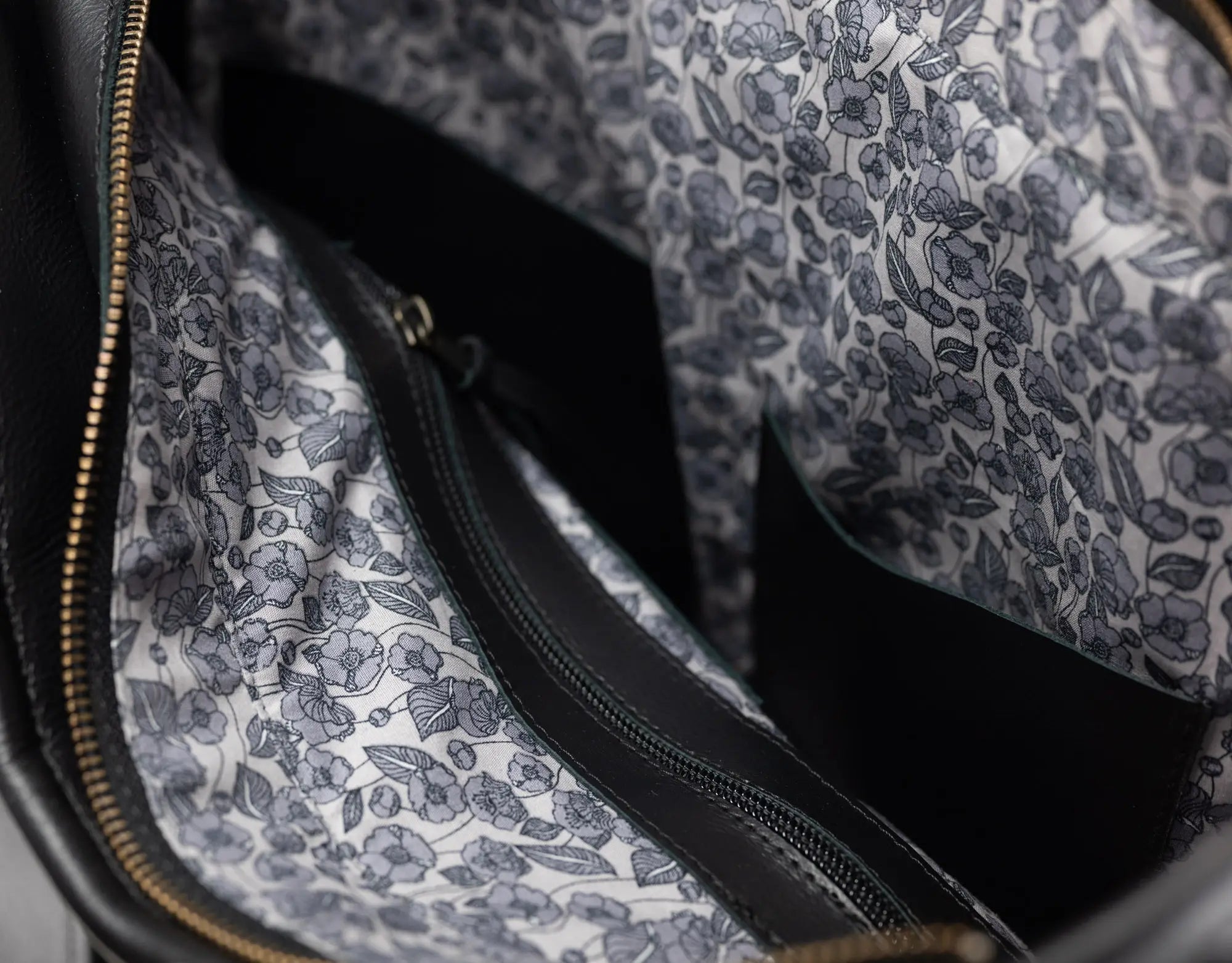 Close-up of the interior of a black bag showing a white fabric lining with a gray floral pattern and a black zipper.