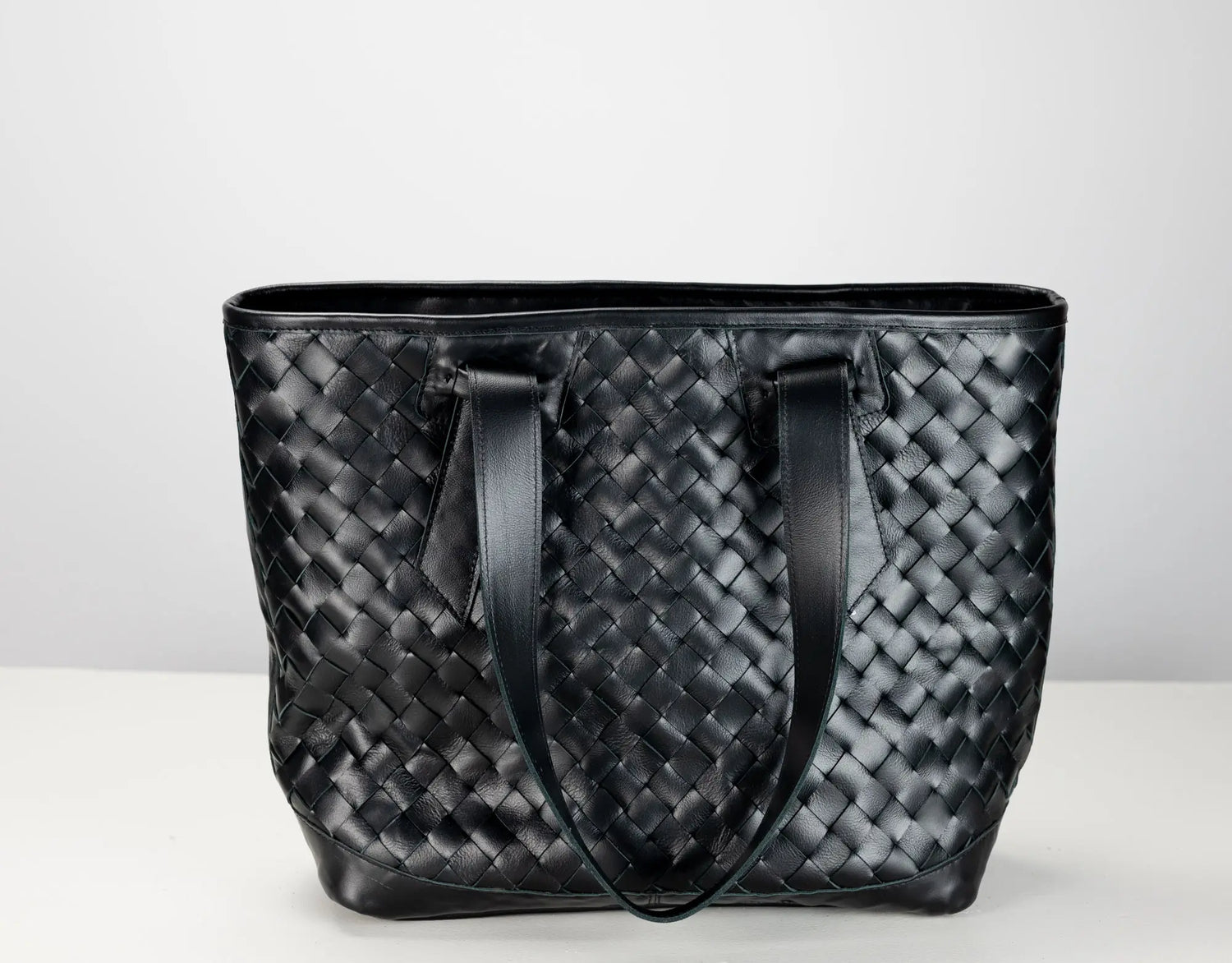 A black woven leather tote bag with two shoulder straps, photographed against a plain light gray background.