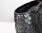 Close-up of a black woven leather boot or shoe showing the textured basketweave pattern and interior lining on a light gray background.
