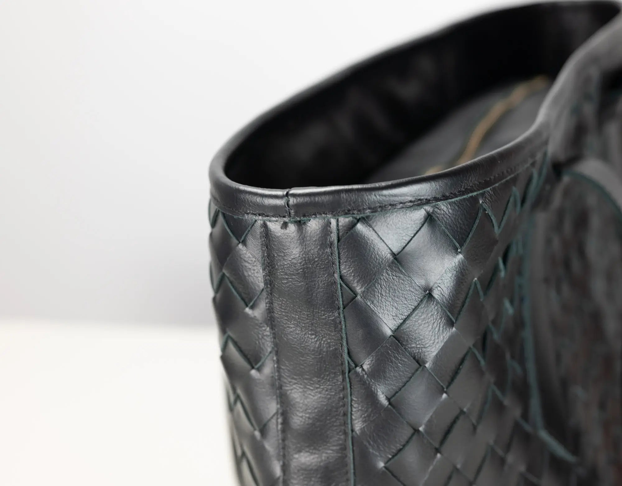 Close-up of a black woven leather boot or shoe showing the textured basketweave pattern and interior lining on a light gray background.