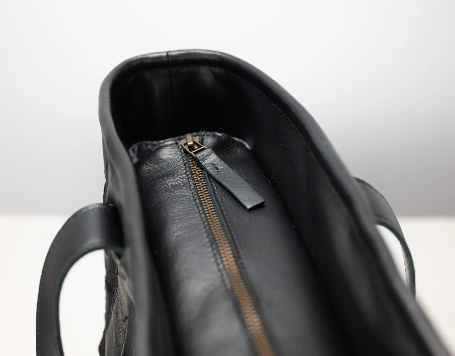 Close-up of a black leather handbag interior showing a black leather zipper pull tab and a gold-tone zipper.