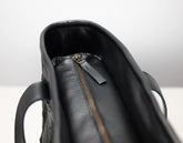 Close-up of a black leather handbag interior showing a black leather zipper pull tab and a gold-tone zipper.