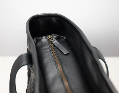 Close-up of a black leather handbag interior showing a black leather zipper pull tab and a gold-tone zipper.