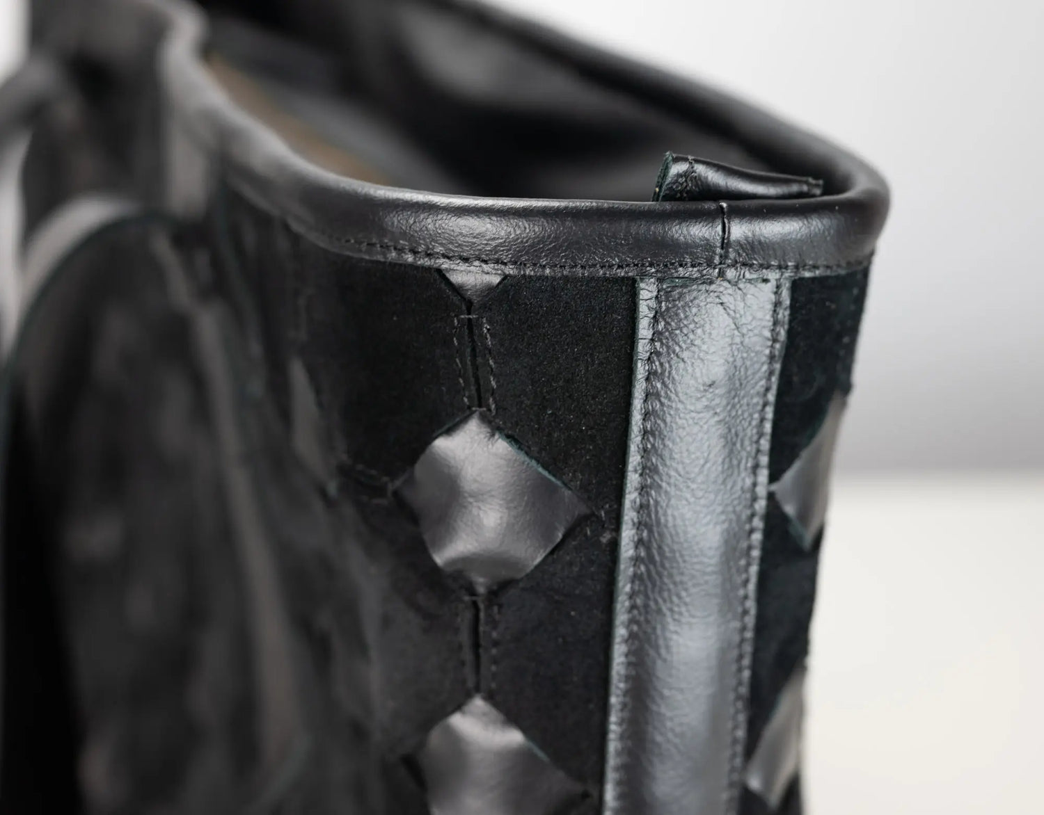Close-up of a black woven leather boot or shoe showing the textured weave, stitched edge, and smooth leather trim.