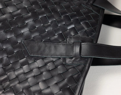 Close-up of a black woven leather bag with a strap detail and textured leather surface.