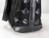 Close-up of a black woven leather handbag showing the textured geometric pattern and dark sole on a white background.
