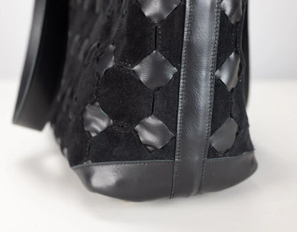 Close-up of a black woven leather handbag showing the textured geometric pattern and dark sole on a white background.