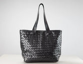 A black woven leather tote bag with two shoulder straps, displayed on a white surface against a light gray background.