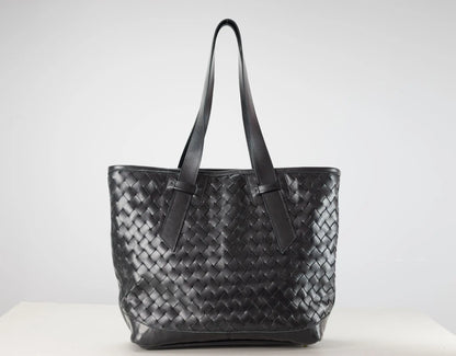 A black woven leather tote bag with two shoulder straps, displayed on a white surface against a light gray background.