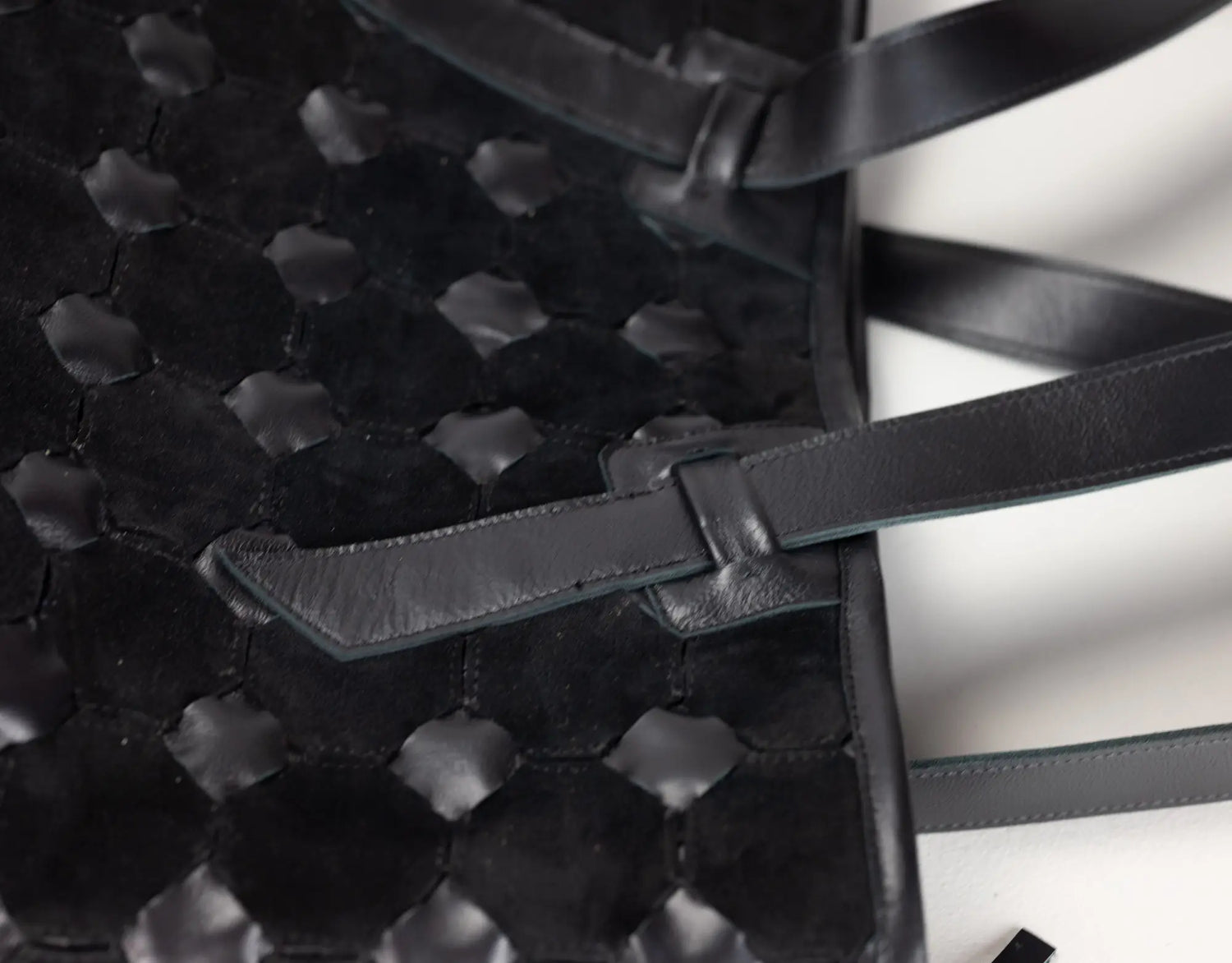 Close-up of a black woven leather handbag with a textured honeycomb pattern and a matching leather strap detail on a white background.