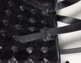 Close-up of a black woven leather handbag with a textured honeycomb pattern and a matching leather strap detail on a white background.