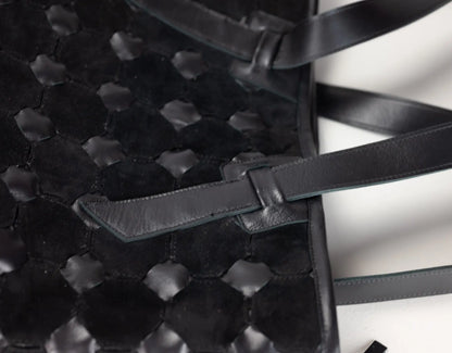 Close-up of a black woven leather handbag with a textured honeycomb pattern and a matching leather strap detail on a white background.