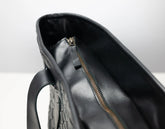Close-up of the interior of a black leather handbag, showing a black zipper with a small pull tab and a textured exterior surface.
