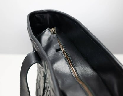 Close-up of the interior of a black leather handbag, showing a black zipper with a small pull tab and a textured exterior surface.