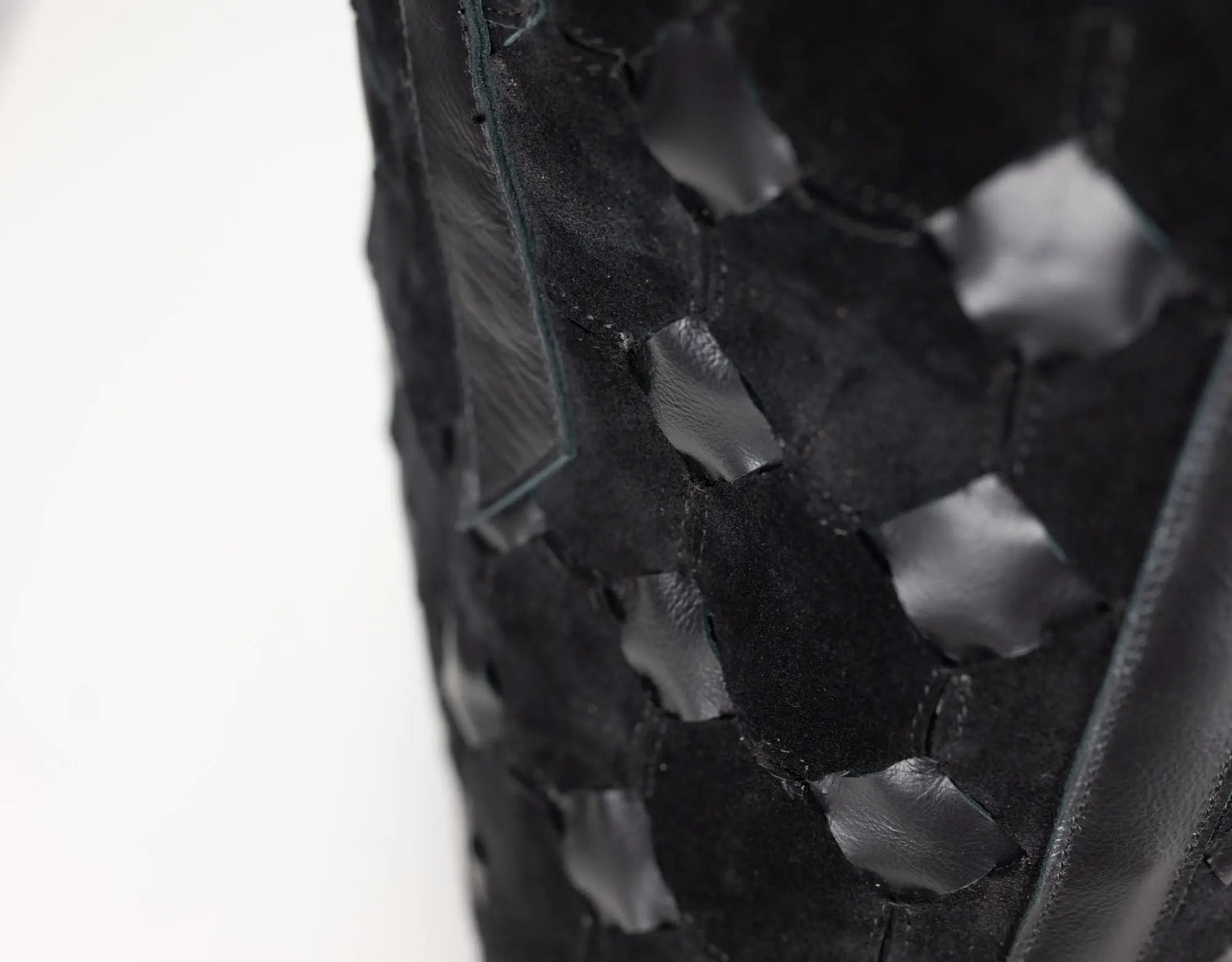 Close-up of a black woven leather bag featuring a distinctive hexagonal cutout pattern, set against a plain white background.