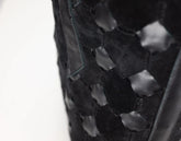 Close-up of a black woven leather bag featuring a distinctive hexagonal cutout pattern, set against a plain white background.