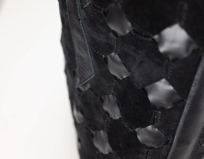 Close-up of a black woven leather bag featuring a distinctive hexagonal cutout pattern, set against a plain white background.