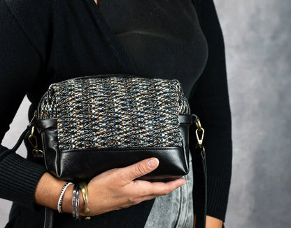 Person holding a black and silver patterned handbag against a gray background