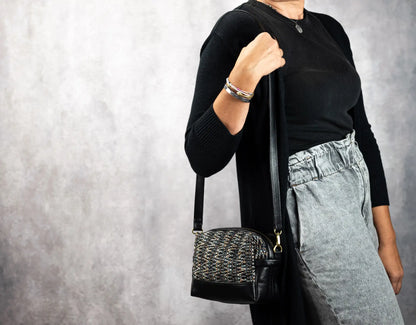 Person holding a black handbag against a gray background