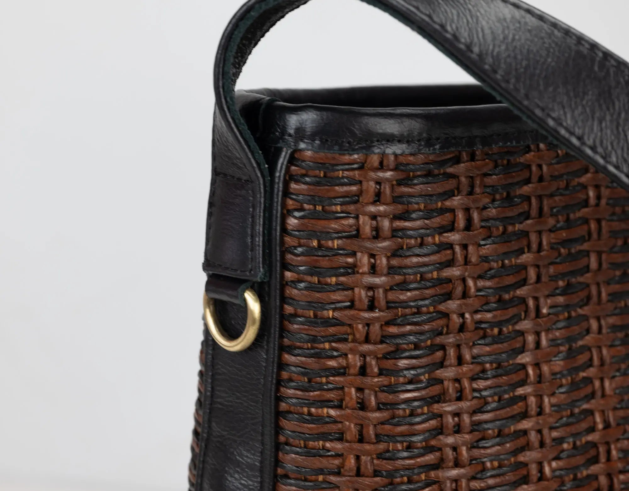 Close-up of a woven handbag with a black strap on a light gray background