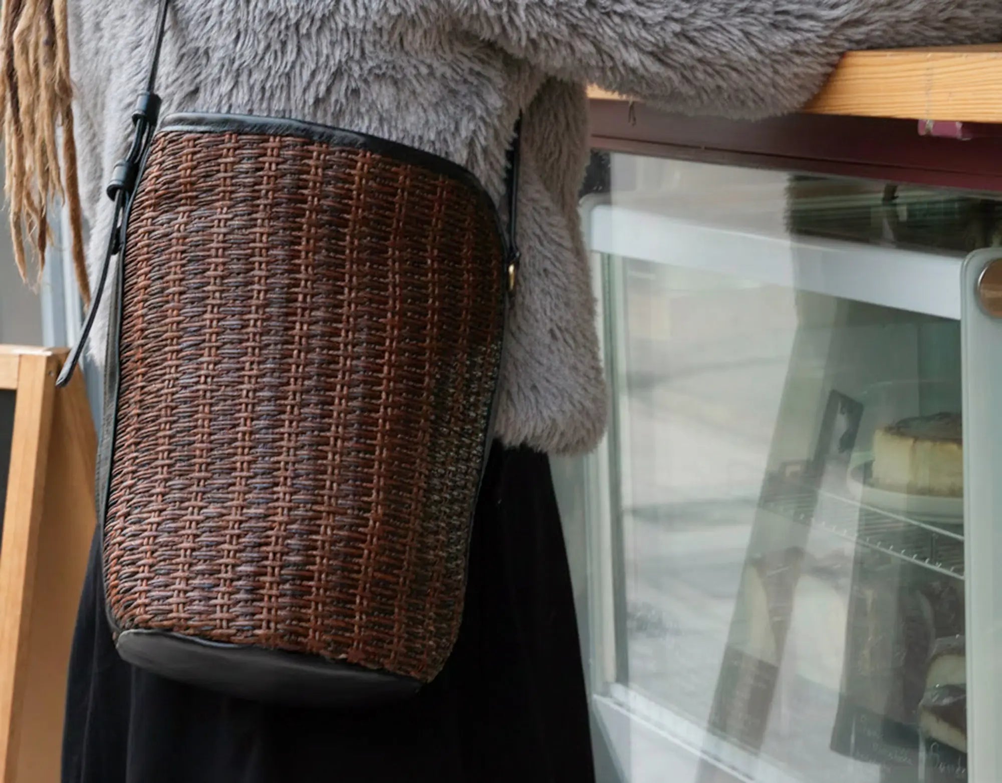 Wicker bag with a textured surface held by a person wearing a gray fluffy coat.